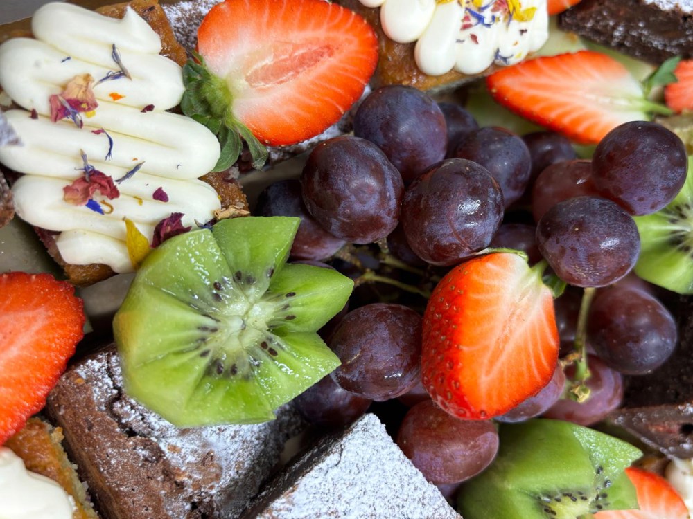 An image showing our seasonal fruit and cake platter including kiwi, strawberries, grapes and cake